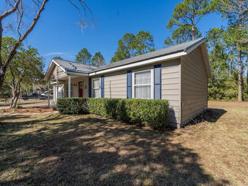 A single-story house with tan siding, blue shutters, and a metal roof sits on grass — 14641 NE 154TH STREET, FORT MC COY, FL