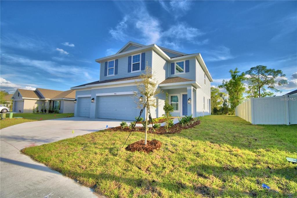 A two-story, light blue suburban house with a three-car garage and a white vinyl fence — 906 SOFIA LANE, DAVENPORT, FL