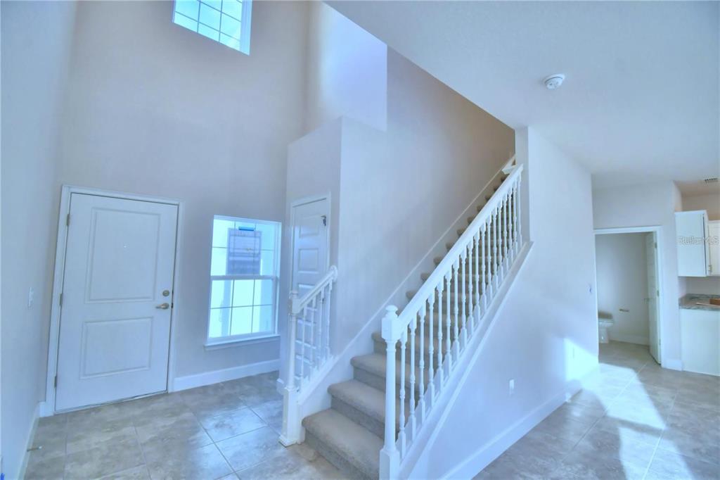 A bright entryway features a high ceiling, tiled floors, and a carpeted staircase with white railings — 906 SOFIA LANE, DAVENPORT, FL