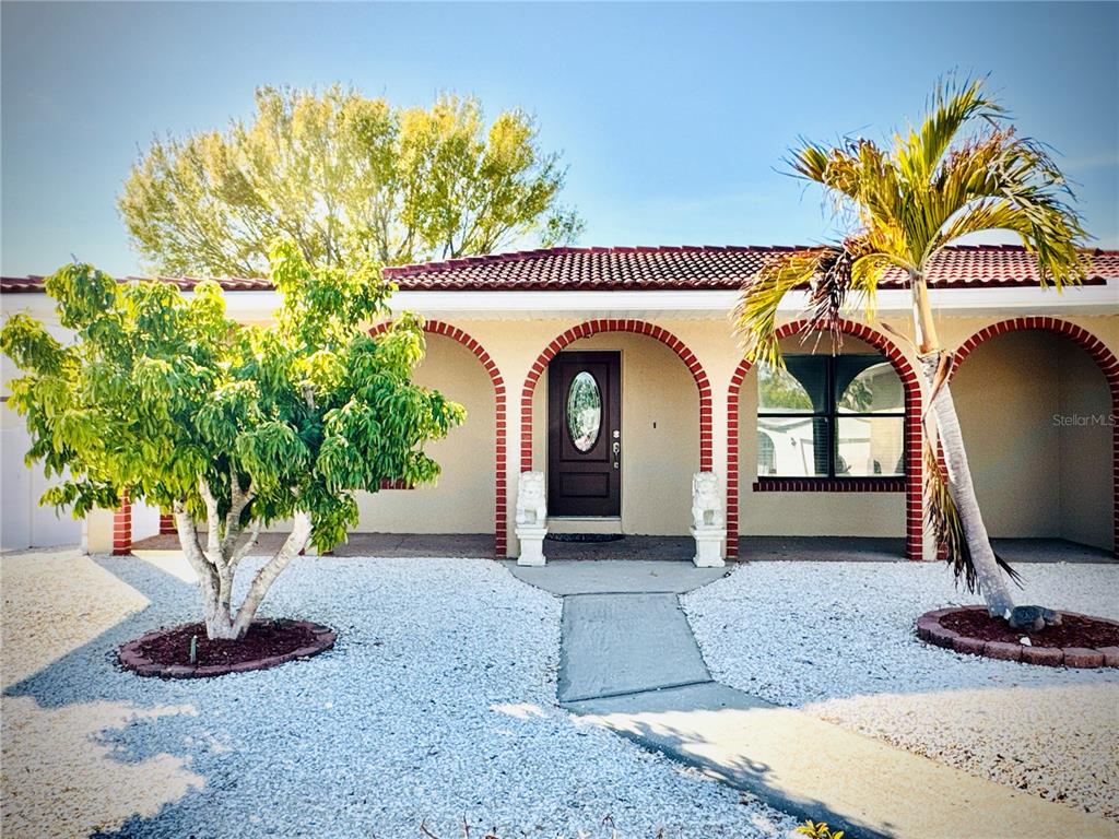 A single-story house exterior features arched brick entryways, a dark front door, and gravel landscaping — 6512 MANILA PALM WAY, APOLLO BEACH, FL