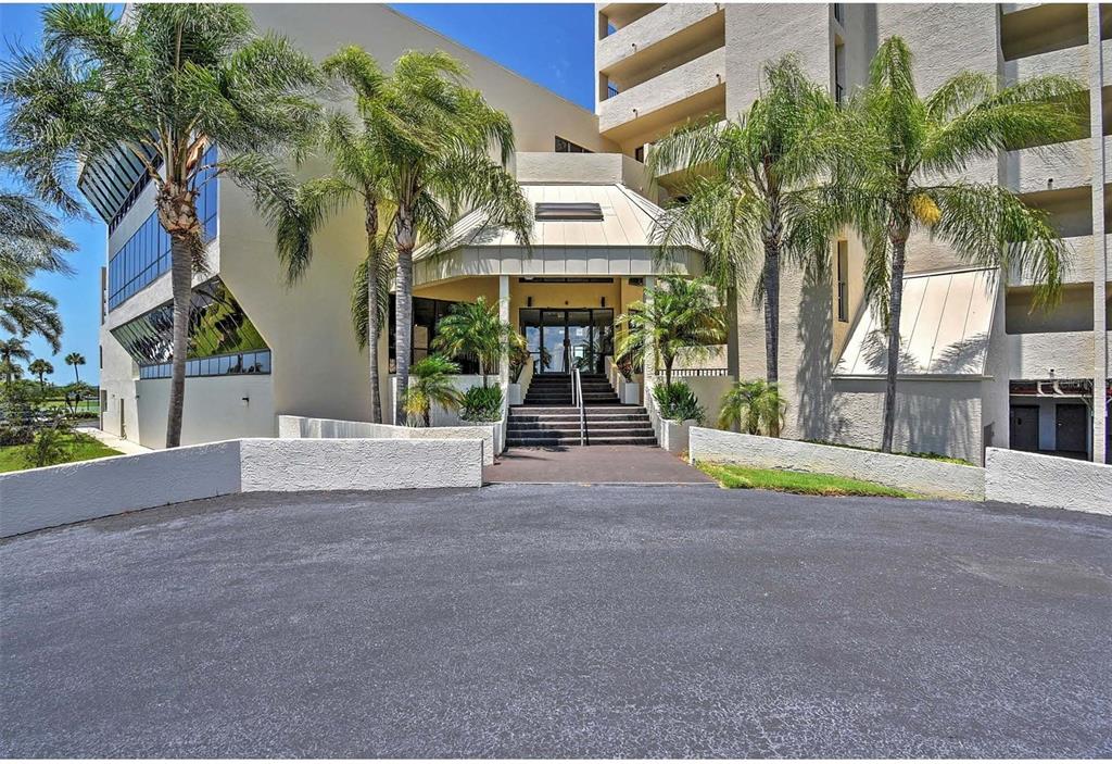 The exterior of a multi-story building features a covered entrance with stairs and palm trees — 5915 SEA RANCH DRIVE UNIT 310, HUDSON, FL