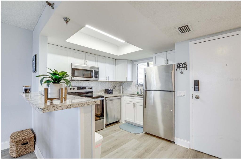 A kitchen features white cabinets, stainless steel appliances, granite countertops, and light wood-look flooring — 5915 SEA RANCH DRIVE UNIT 310, HUDSON, FL
