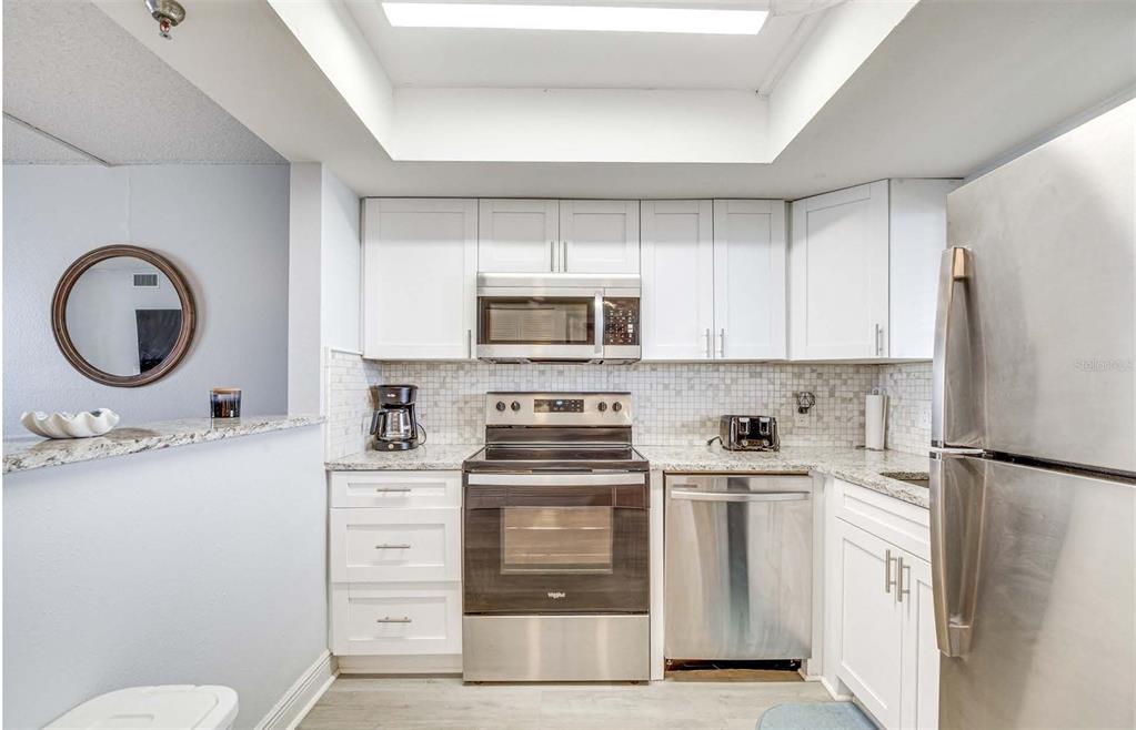 A kitchen features white cabinets, stainless steel appliances, granite countertops, and a tiled backsplash — 5915 SEA RANCH DRIVE UNIT 310, HUDSON, FL