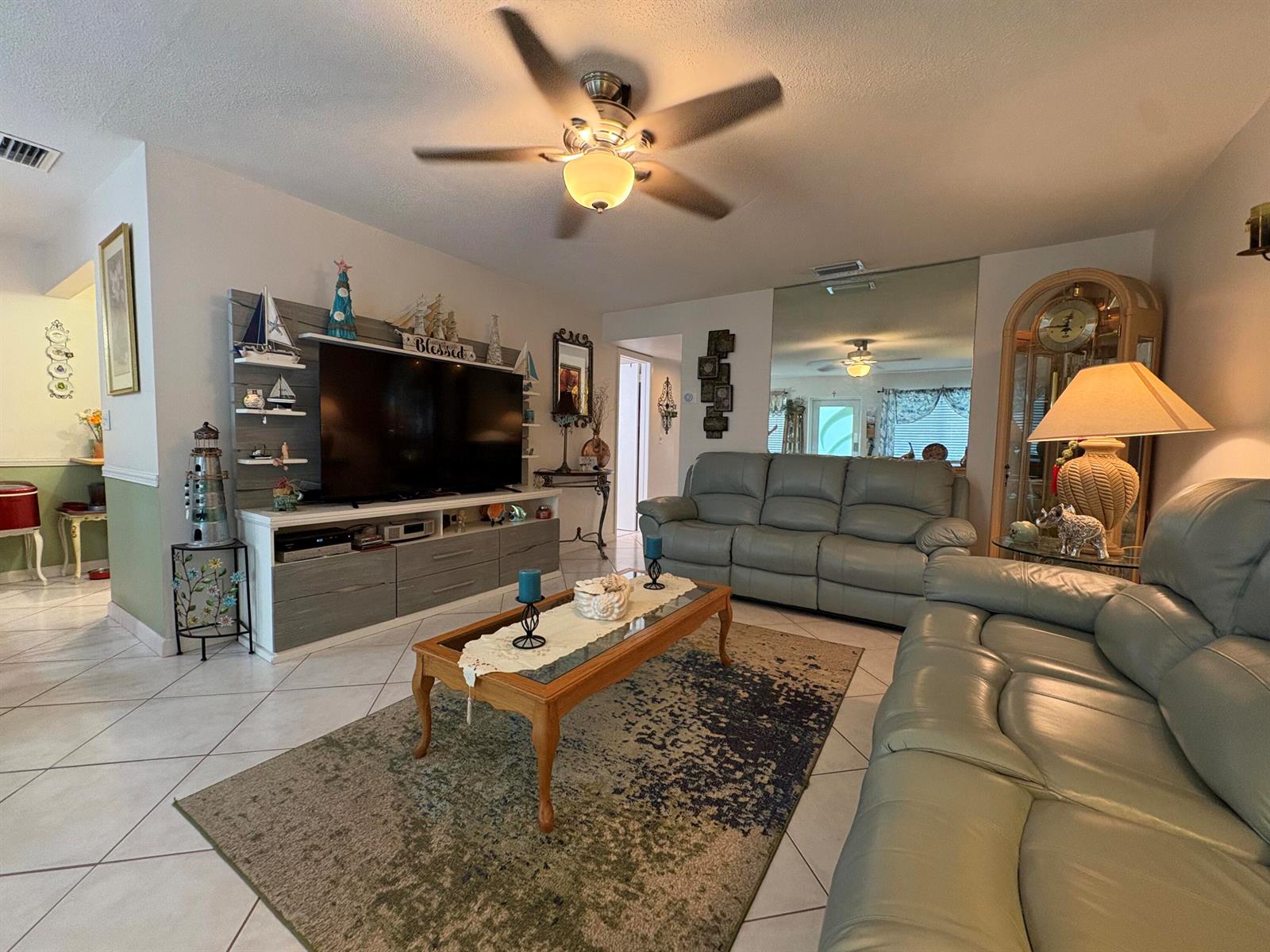 A living room features light-colored leather sofas, a wood coffee table, and a large television — 175 Bedford # G, West Palm Beach FL 33417, WEST PALM BEACH, FL