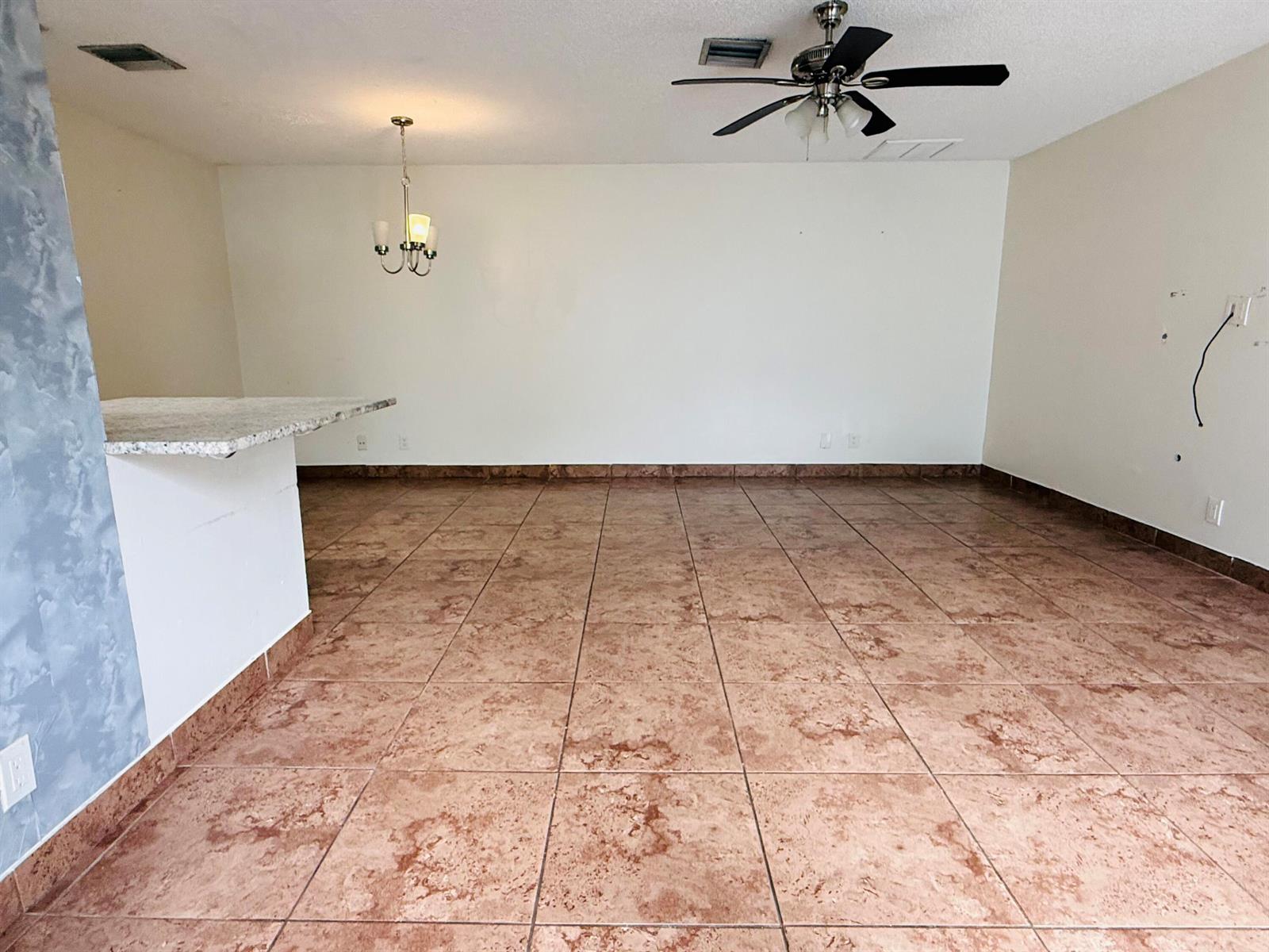 An empty room features brown tile flooring, a ceiling fan, and a kitchen breakfast bar — 21 Crossings Circle # C, Boynton Beach FL 33435, BOYNTON BEACH, FL