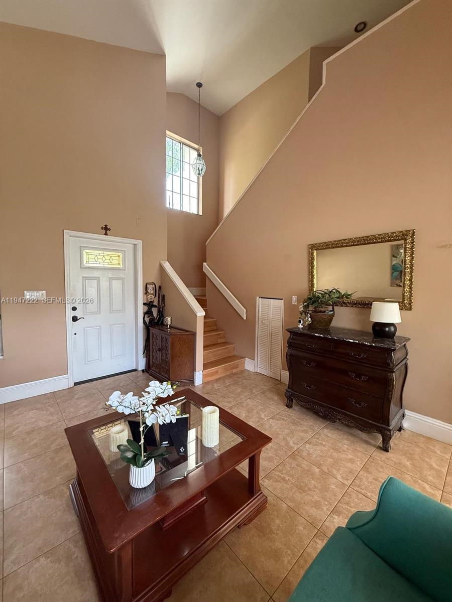 A high-ceilinged foyer features tile flooring, a staircase, a wooden chest, and a coffee table — 14534 SW 144th Ter, Miami FL 33186, MIAMI, FL
