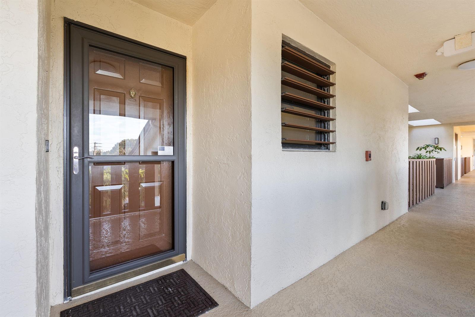 A brown storm door and a louvered window are on a beige exterior hallway wall — 160 SE Saint Lucie Boulevard # 402a, Stuart FL 34996, STUART, FL