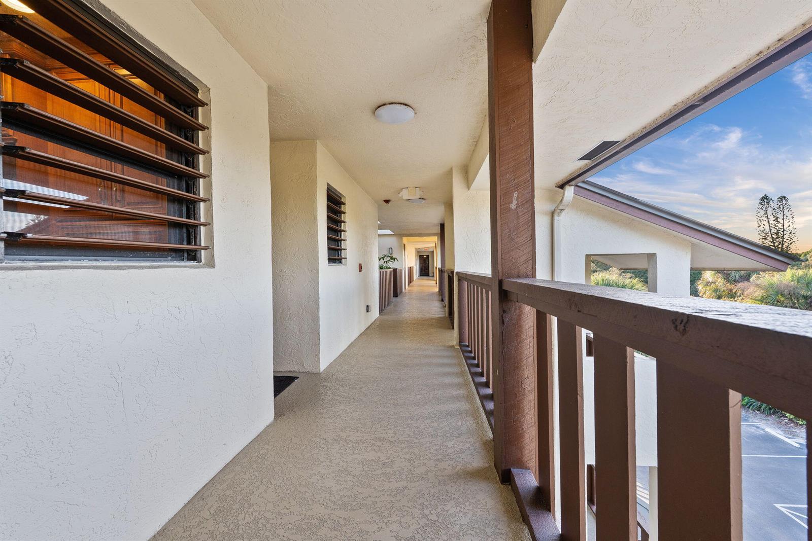 An outdoor apartment hallway features a textured floor, wooden railings, and louvered windows — 160 SE Saint Lucie Boulevard # 402a, Stuart FL 34996, STUART, FL