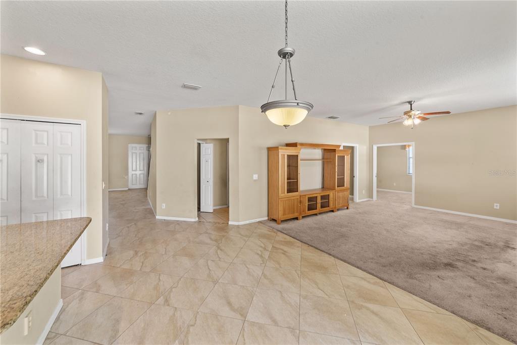 A living area with tile flooring, carpeted space, a wooden entertainment center, and a pendant light — 6110 39TH COURT E, BRADENTON, FL