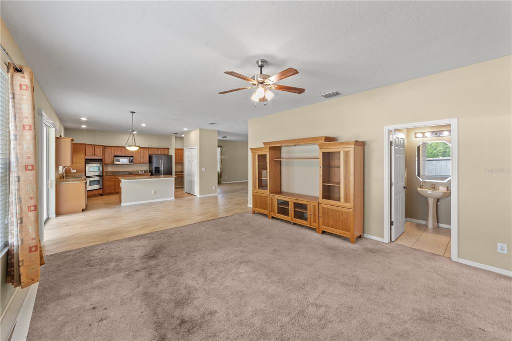 A living room with carpeted floors and a wooden entertainment center opens to a kitchen — 6110 39TH COURT E, BRADENTON, FL