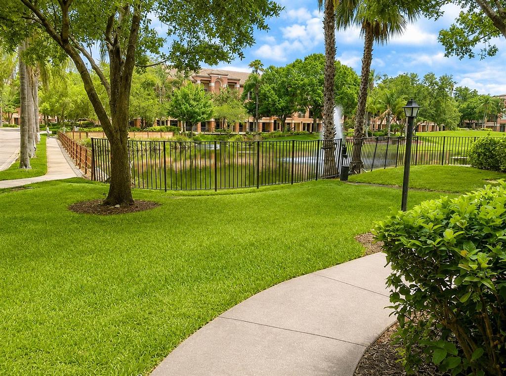 A grassy lawn with a curved walkway leads to a fenced pond and apartment building — 614 ARBOR LAKE LANE UNIT 614, TAMPA, FL