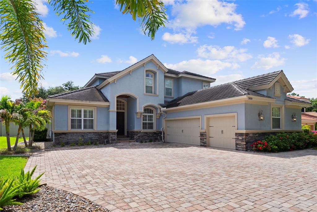 A two-story blue house with a stone base, tiled roof, and a paved driveway — 2689 WATERS EDGE COURT, DUNEDIN, FL