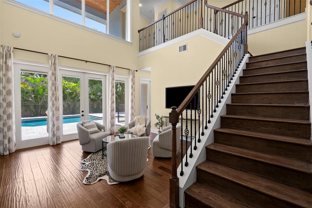 A living area with a staircase, hardwood floors, and glass doors overlooking a swimming pool — 2689 WATERS EDGE COURT, DUNEDIN, FL