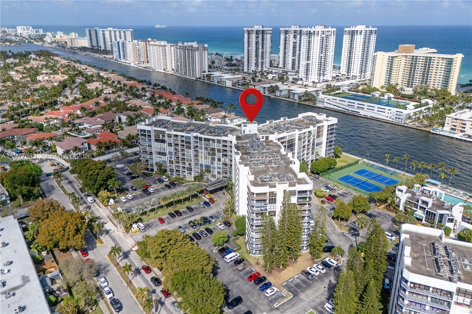 An aerial view shows a multi-story apartment building with a parking lot and tennis courts — 1000 Parkview Dr # 222, Hallandale Beach FL 33009, HALLANDALE BEACH, FL