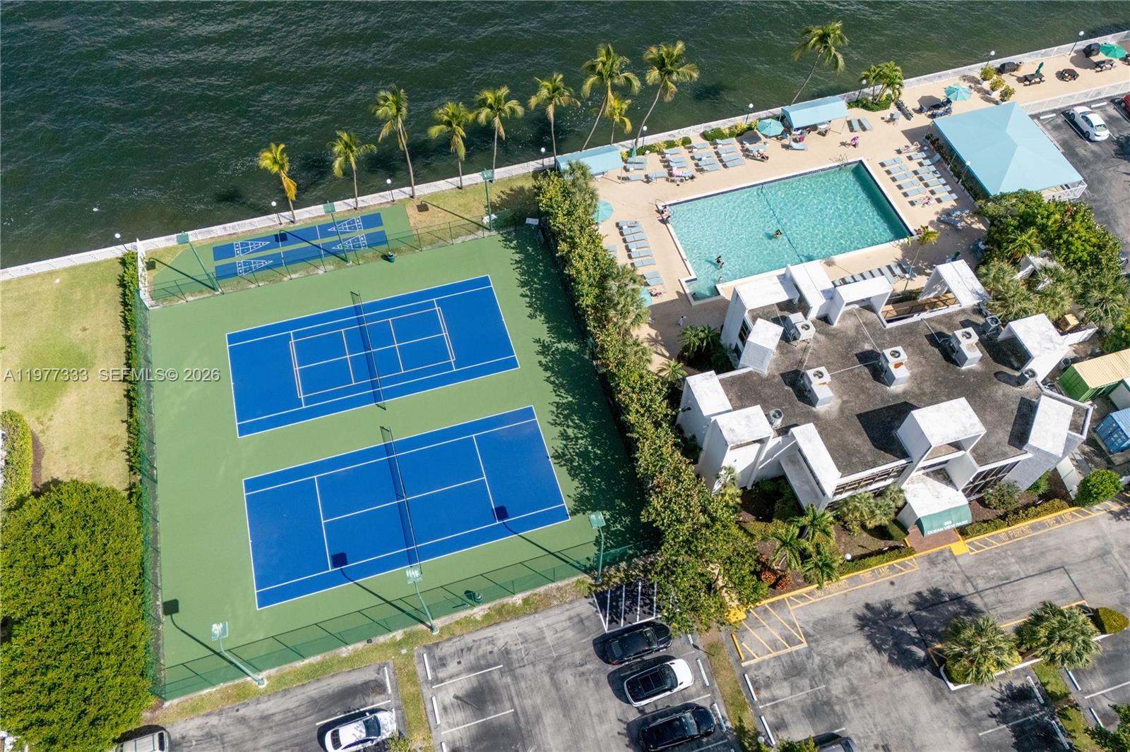An aerial view shows two tennis courts, a swimming pool, and a building near water — 1000 Parkview Dr # 222, Hallandale Beach FL 33009, HALLANDALE BEACH, FL