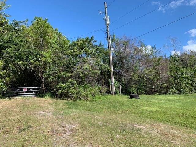 A utility pole stands in a grassy field next to a metal gate and trees — 1290 CINDER LANE, KISSIMMEE, FL