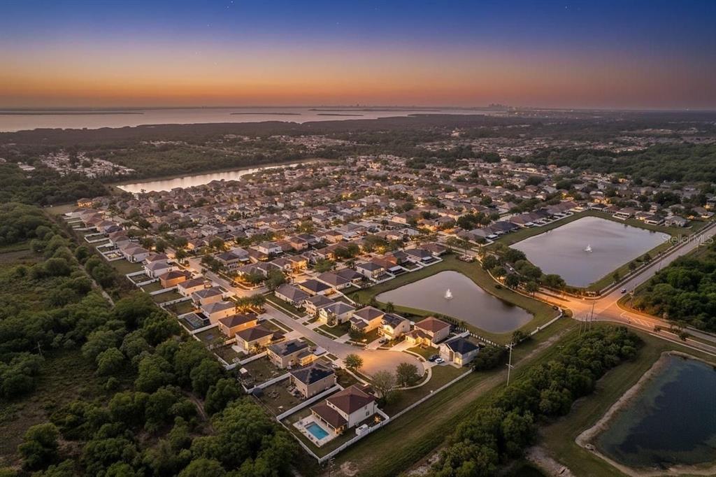 An aerial view of a suburban neighborhood at sunset featuring houses, ponds, and surrounding woods — 12136 TREE HAVEN AVENUE, GIBSONTON, FL