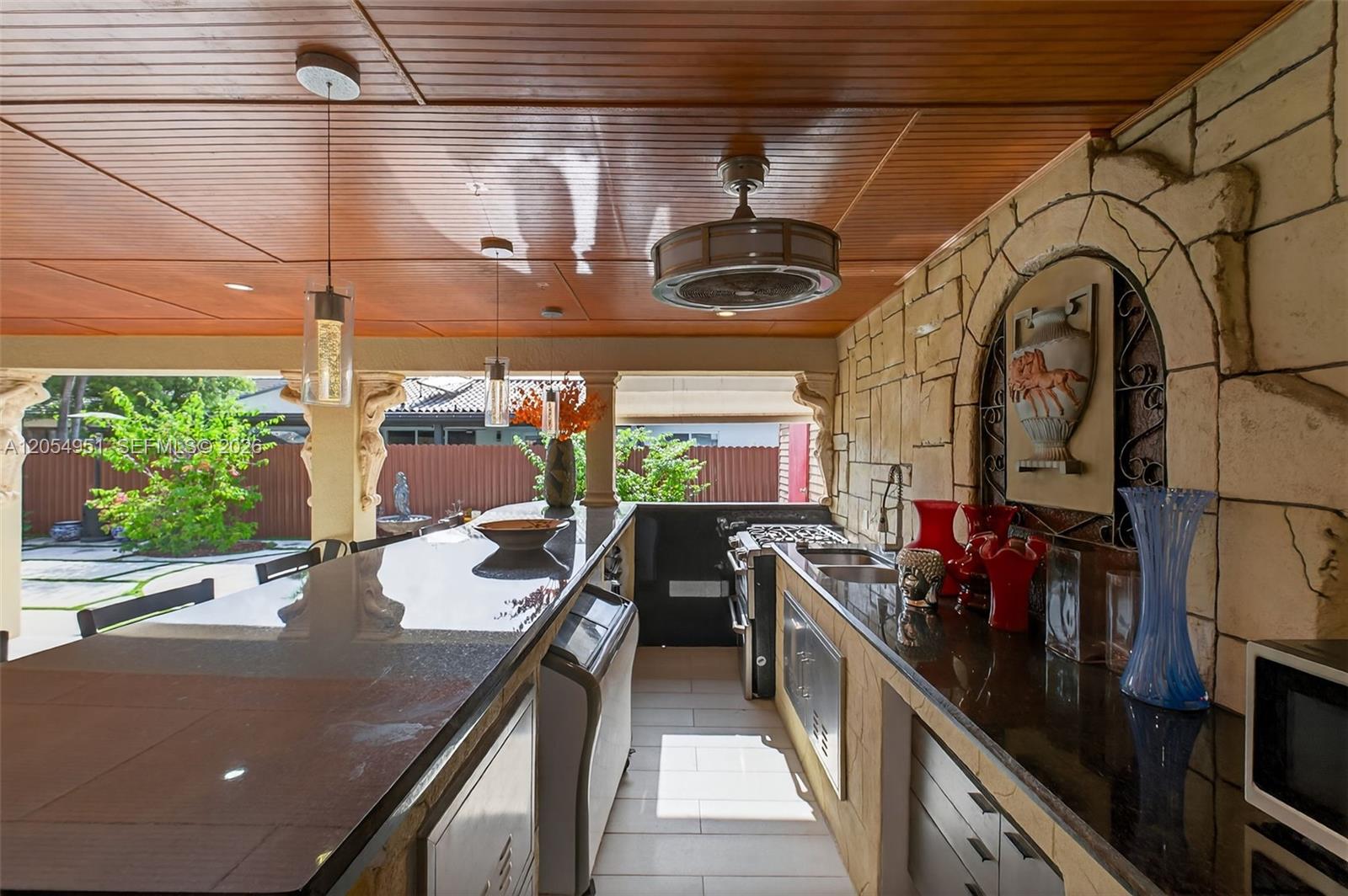 An outdoor kitchen features a stone wall, dark countertops, stainless steel appliances, and wood ceilings — 2431 SW 127th Ave # 2431, Miami FL 33175, MIAMI, FL
