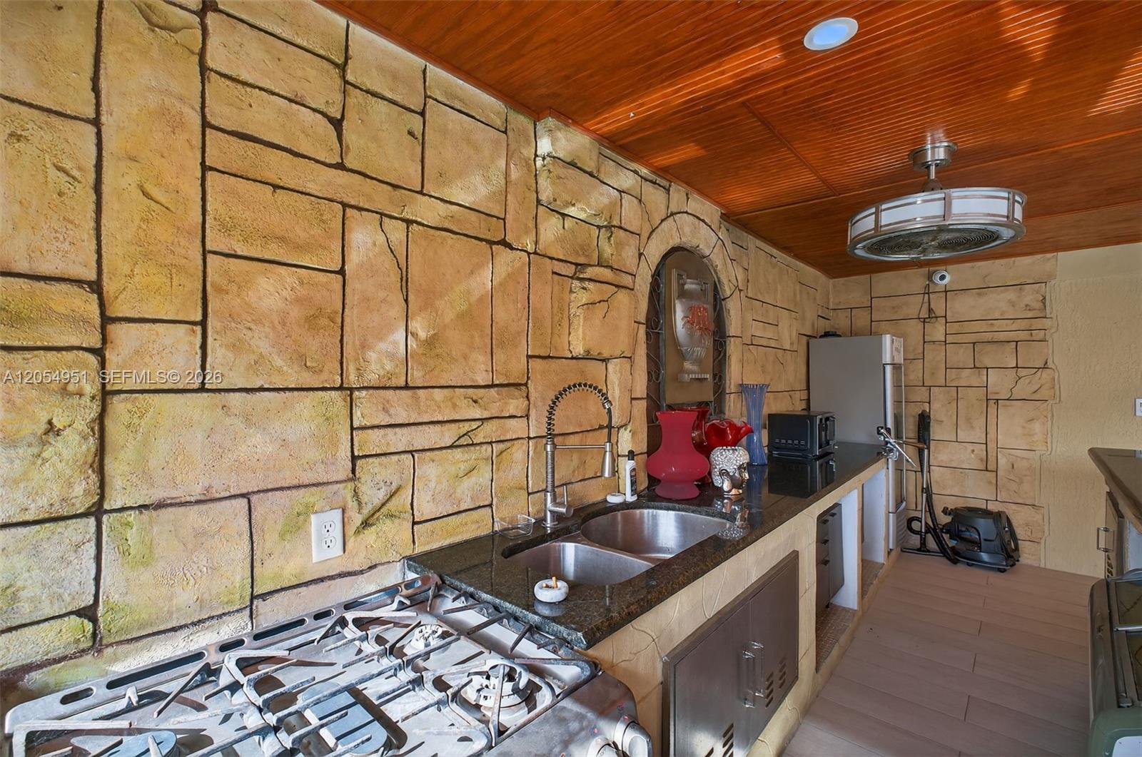 An outdoor kitchen features stone-patterned walls, a wooden ceiling, a gas stove, and a sink — 2431 SW 127th Ave # 2431, Miami FL 33175, MIAMI, FL