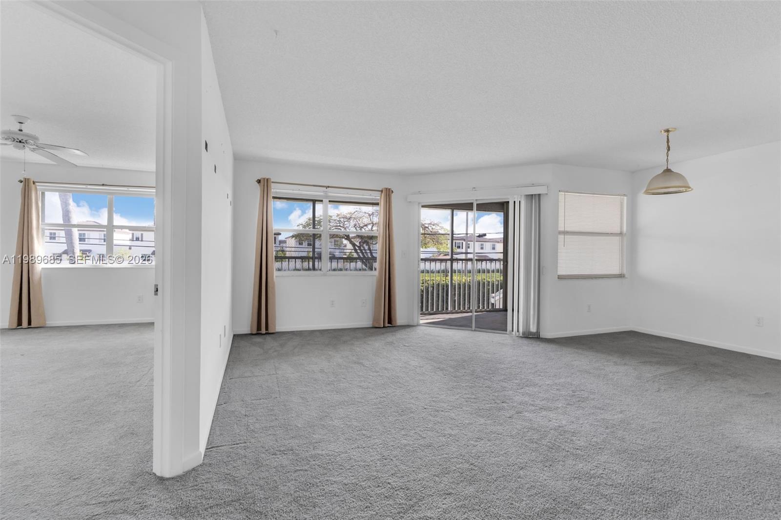 An empty living room features gray carpeting, white walls, and a sliding glass balcony door — 2274 SE 27th Dr # F, Homestead FL 33035, HOMESTEAD, FL