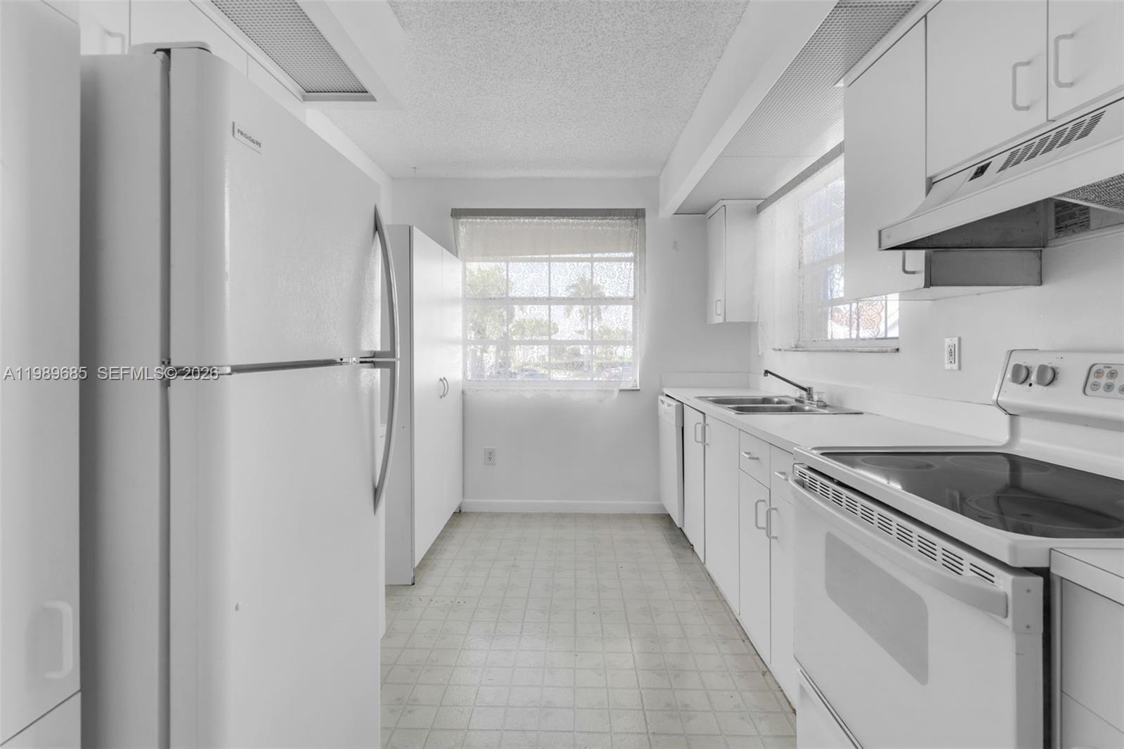 A white kitchen features a refrigerator, electric range, double sink, and vinyl flooring — 2274 SE 27th Dr # F, Homestead FL 33035, HOMESTEAD, FL