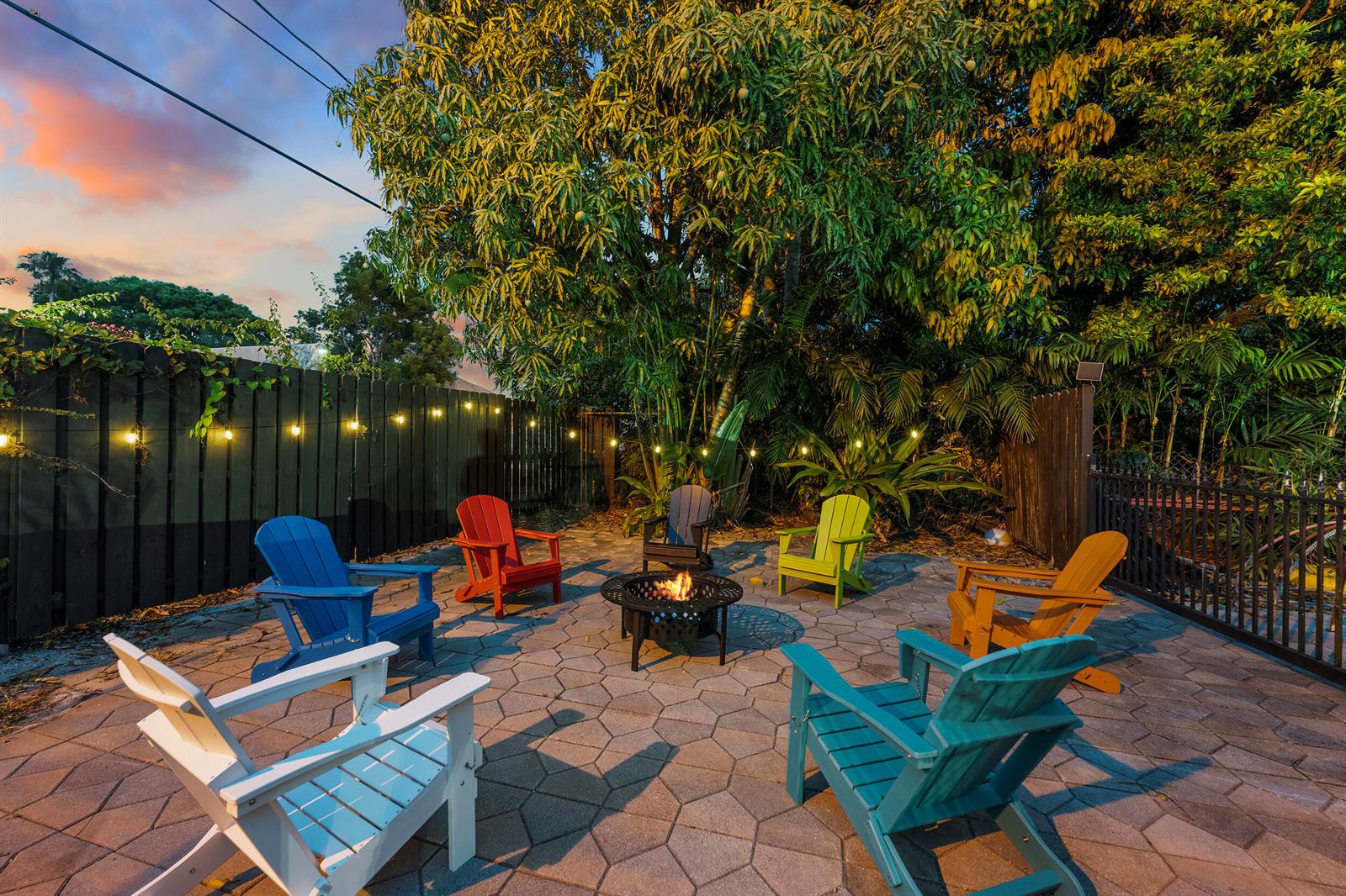 A backyard patio features a fire pit surrounded by colorful Adirondack chairs under string lights — 643 36th Street, West Palm Beach FL 33407, WEST PALM BEACH, FL