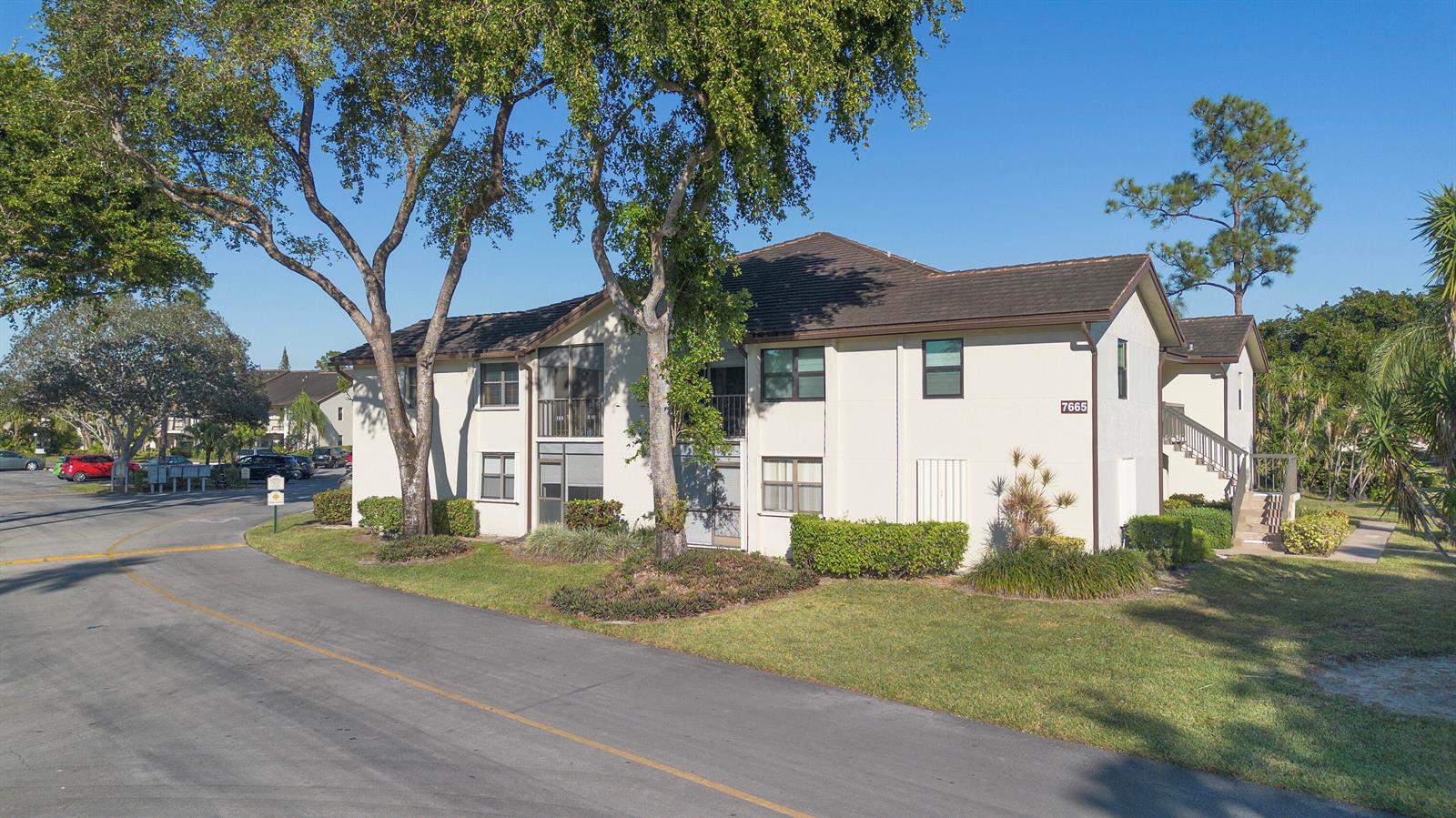A two-story apartment building with a beige exterior, dark roof, and surrounding landscaping — 7665 Tahiti Lane # 102, Lake Worth FL 33467, LAKE WORTH, FL