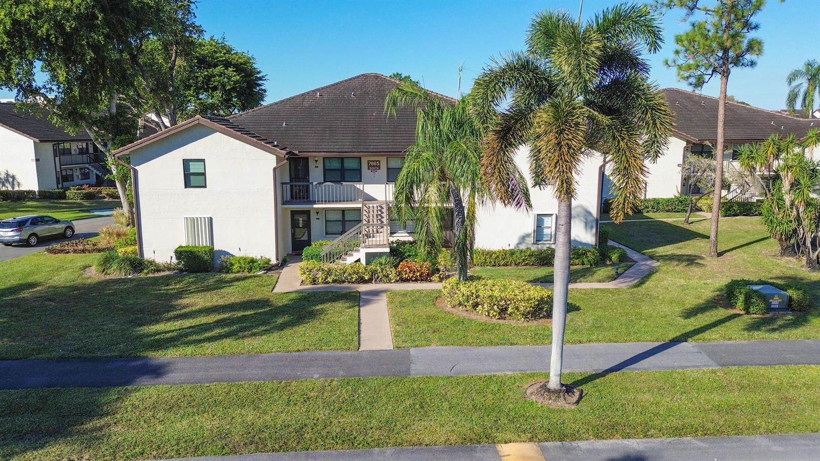 An exterior view of a two-story apartment building with a palm tree and lawn — 7665 Tahiti Lane # 102, Lake Worth FL 33467, LAKE WORTH, FL