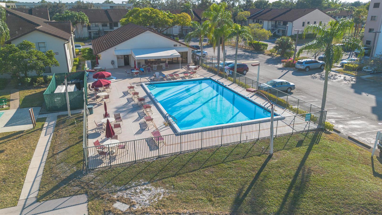 An aerial view shows a rectangular swimming pool surrounded by a patio and metal fence — 7665 Tahiti Lane # 102, Lake Worth FL 33467, LAKE WORTH, FL