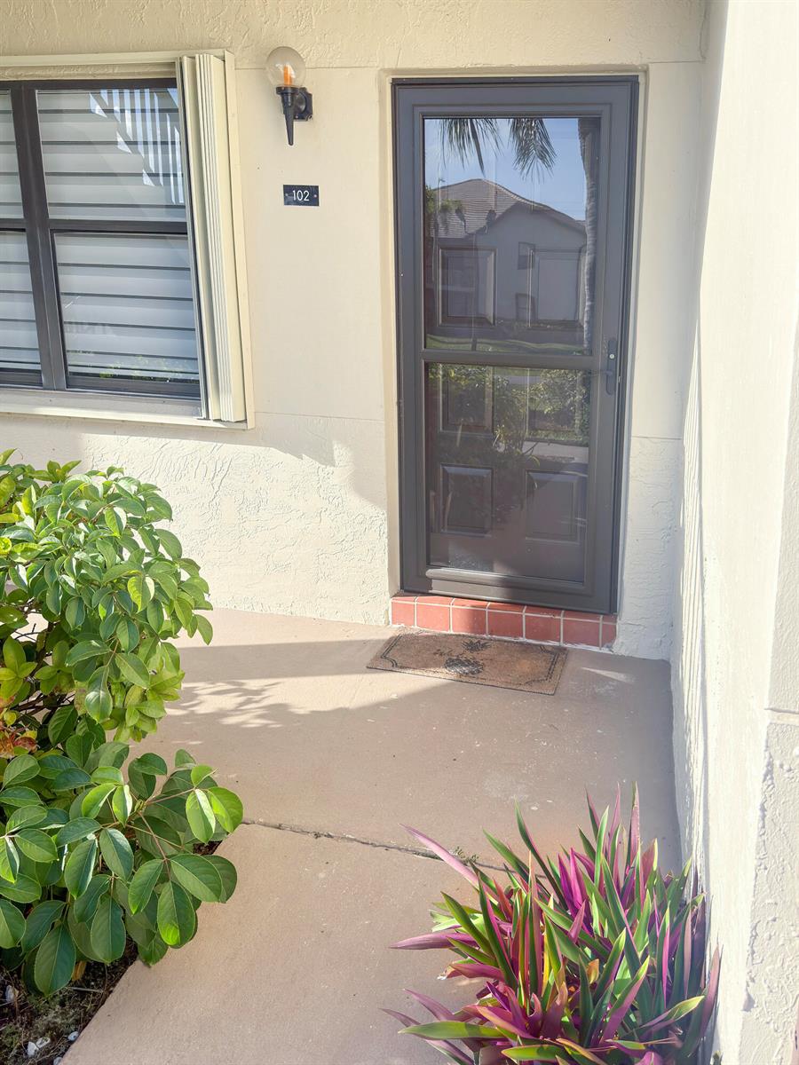 An exterior view of a residential entrance with a dark storm door and unit number — 7665 Tahiti Lane # 102, Lake Worth FL 33467, LAKE WORTH, FL