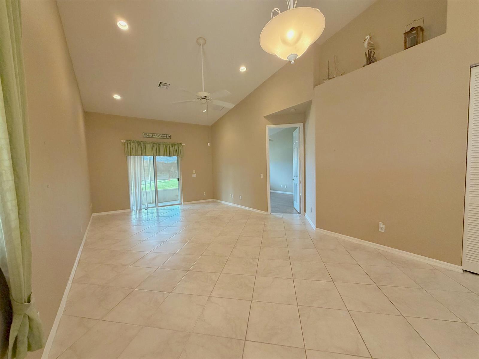 An empty living room features beige tile flooring, vaulted ceilings, and a sliding glass door — 6510 Oxford Circle # 101, Vero Beach FL 32966, VERO BEACH, FL