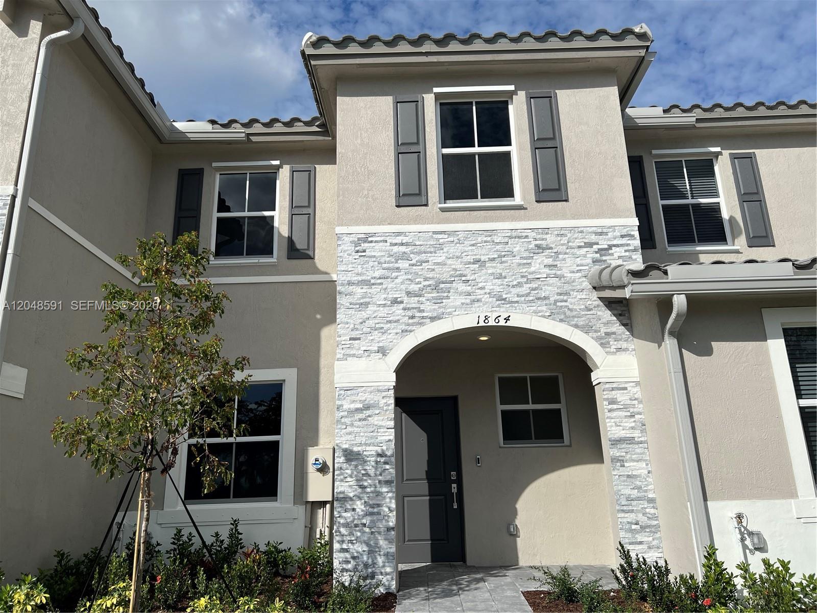 A two-story townhouse exterior features beige stucco walls, gray shutters, and a stone-veneer entryway — 1864 SE 27th Rd, Homestead FL 33035, HOMESTEAD, FL