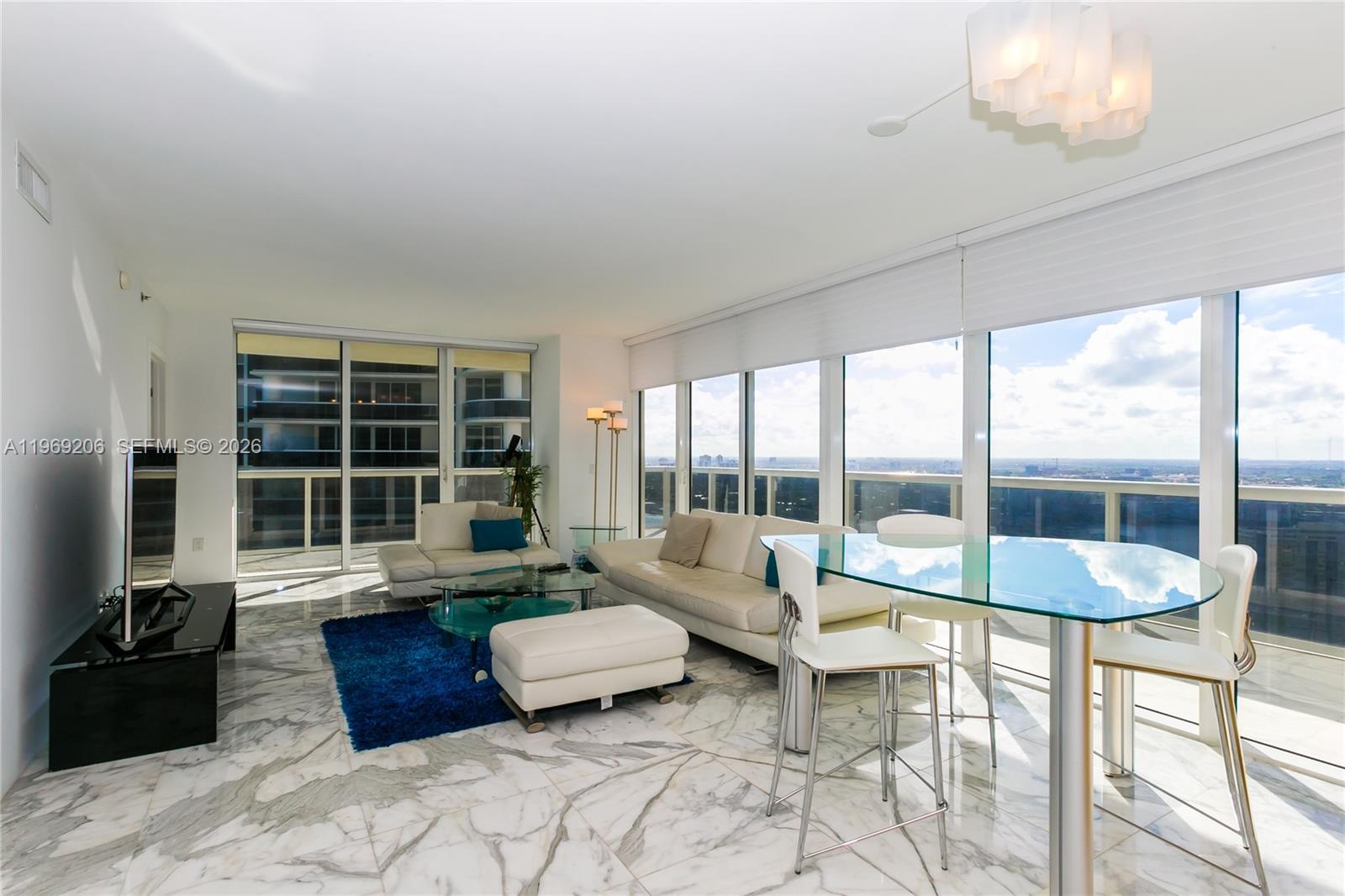 A modern living and dining room features marble floors, white furniture, and floor-to-ceiling windows — 1830 S OCEAN DR # 2906, Hallandale Beach FL 33009, HALLANDALE BEACH, FL