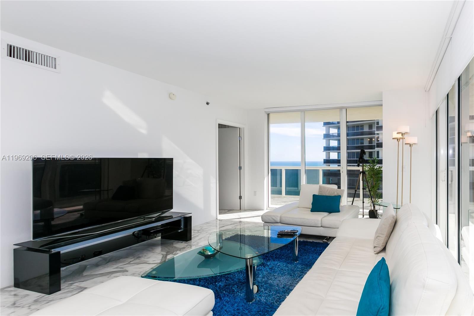 A modern living room features white leather furniture, a glass coffee table, and ocean views — 1830 S OCEAN DR # 2906, Hallandale Beach FL 33009, HALLANDALE BEACH, FL