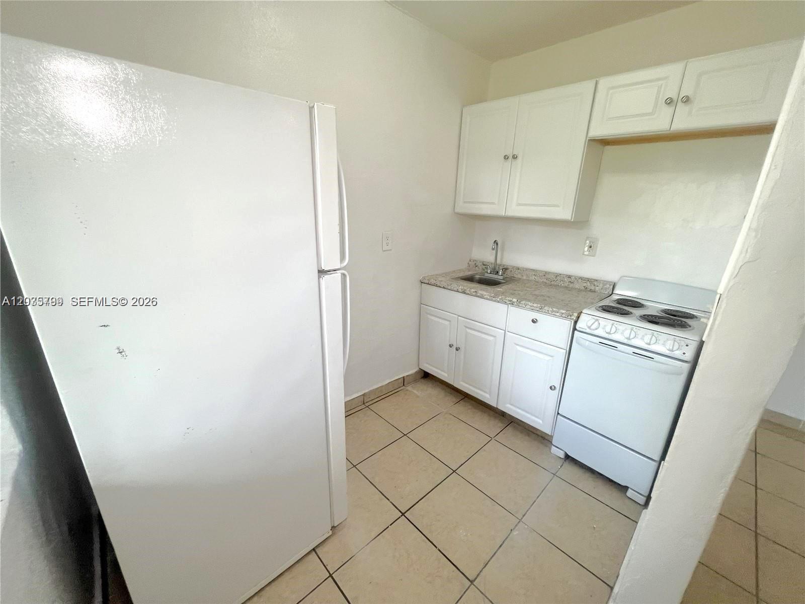 A small kitchen features white cabinets, a white refrigerator, and a white electric stove — 420 NW 10th St # 7, Miami FL 33136, MIAMI, FL