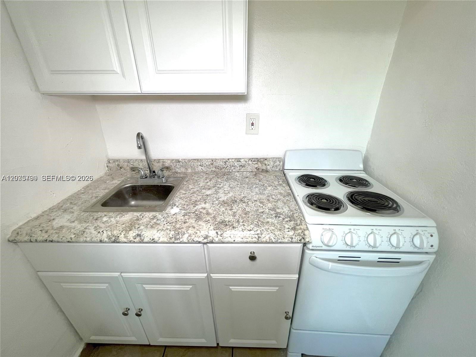 A small kitchen features white cabinets, a granite-look countertop, a stainless steel sink, and a stove — 420 NW 10th St # 7, Miami FL 33136, MIAMI, FL