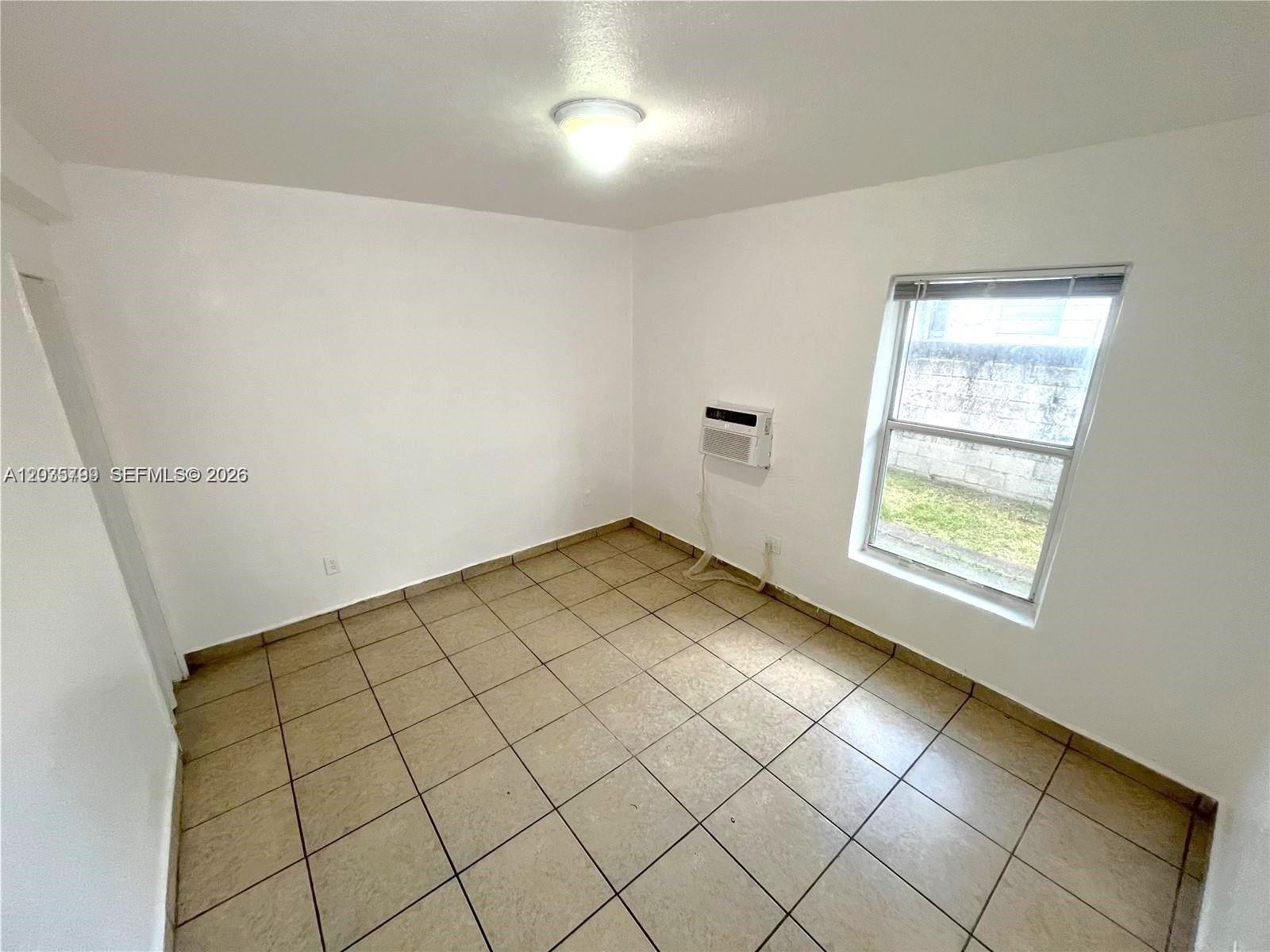 An empty room features white walls, tiled flooring, a window, and a wall-mounted air conditioner — 420 NW 10th St # 7, Miami FL 33136, MIAMI, FL