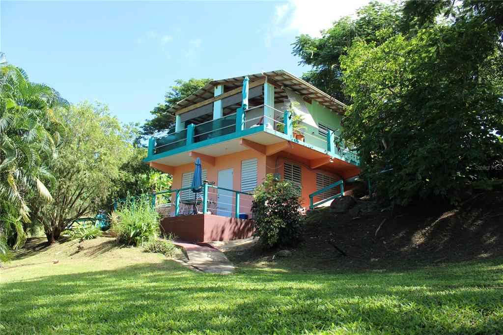 A two-story house with a peach exterior, teal railings, and a balcony sits on grass — 15 BIRD'S NEST STUDIOS, VIEQUES, PR