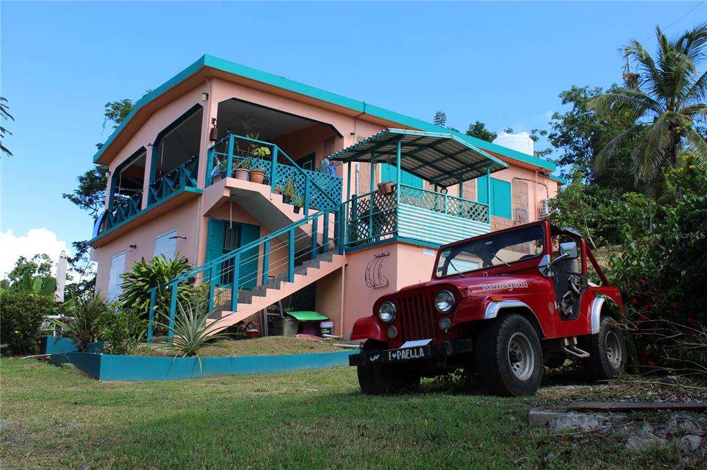 A two-story peach-colored house with a red Jeep parked on the lawn in front — 15 BIRD'S NEST STUDIOS, VIEQUES, PR