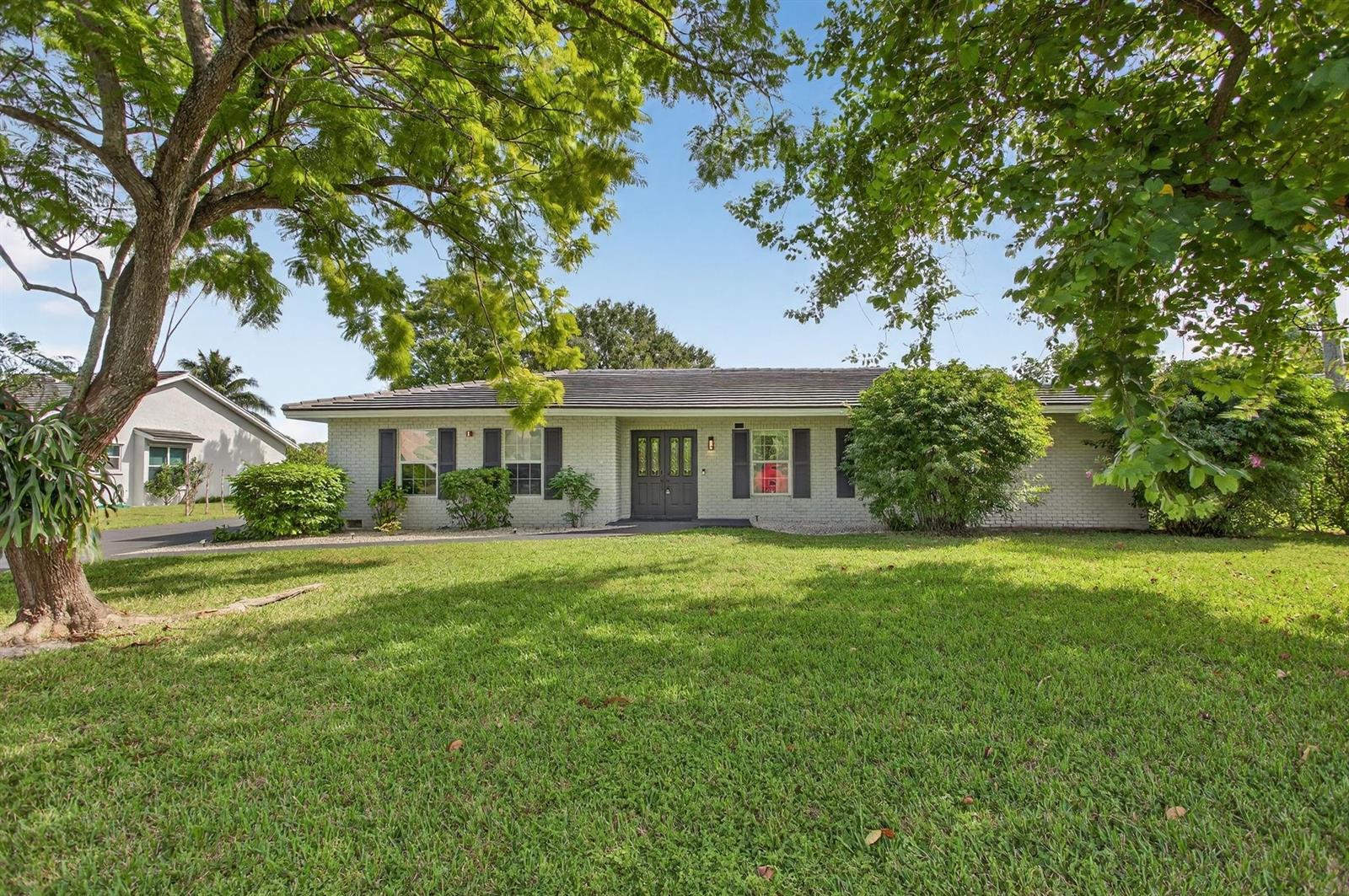 A single-story brick house with a dark front door sits behind a large green lawn — 2421 NW 114th Avenue, Coral Springs FL 33065, CORAL SPRINGS, FL