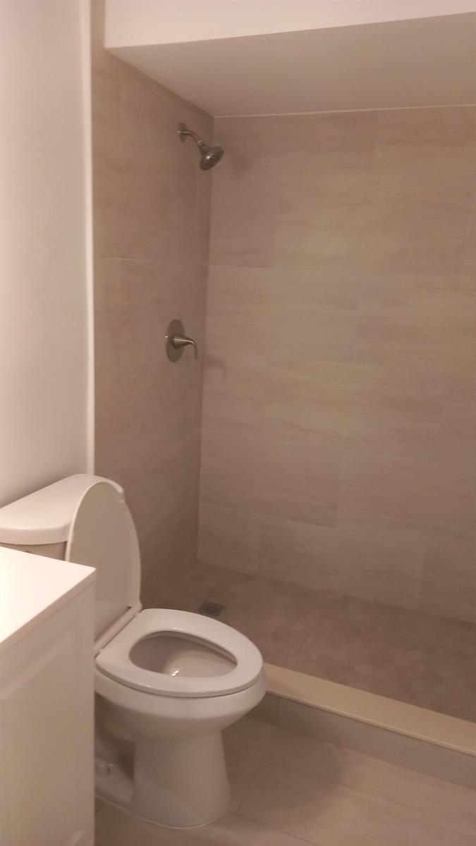 A bathroom features a white toilet next to a walk-in shower with beige tiled walls — 4165 SW 67th Avenue # 208b, Davie FL 33314, DAVIE, FL