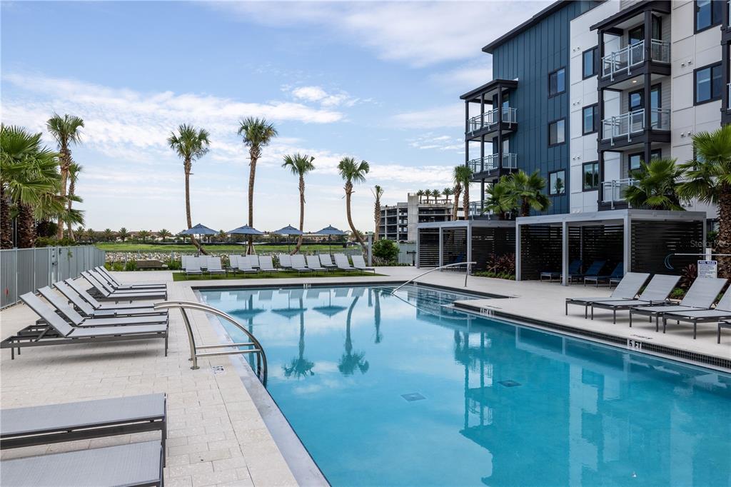 A swimming pool with lounge chairs on a patio next to a modern apartment building — 5127 W TYSON AVENUE UNIT TH2, TAMPA, FL