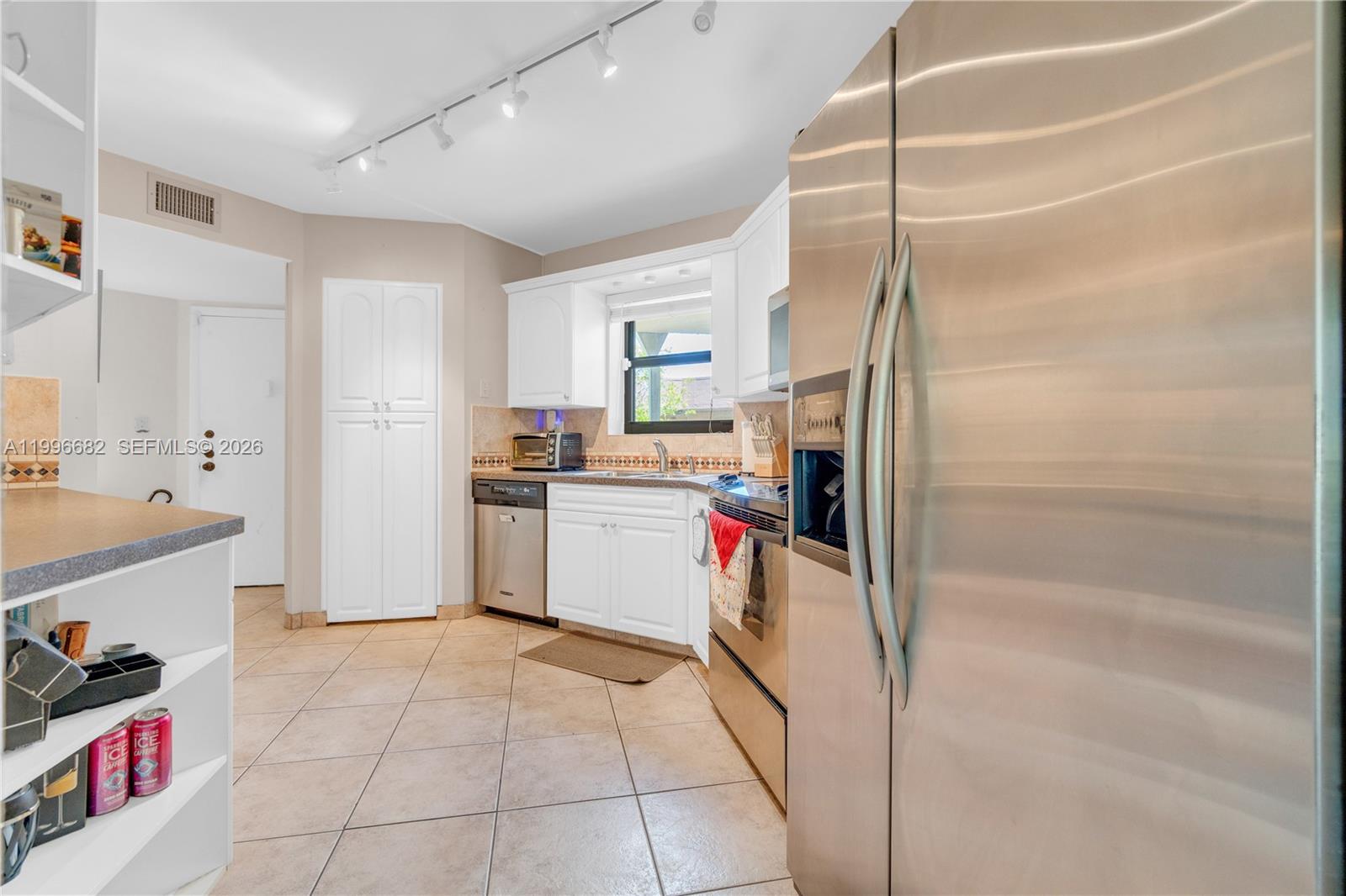 A kitchen features white cabinets, stainless steel appliances, tile flooring, and track lighting — 6755 W Broward Blvd # 405, Plantation FL 33317, PLANTATION, FL