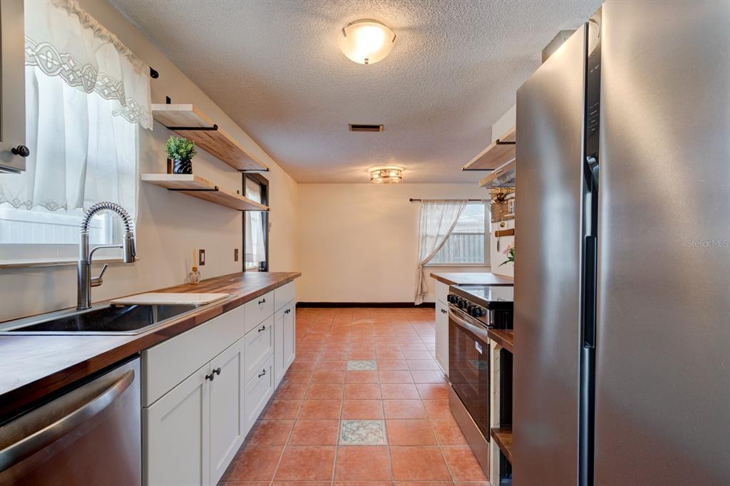 A kitchen features white cabinets, wood countertops, open shelving, stainless steel appliances, and tile flooring — 119 BIGELOW DRIVE, EDGEWATER, FL