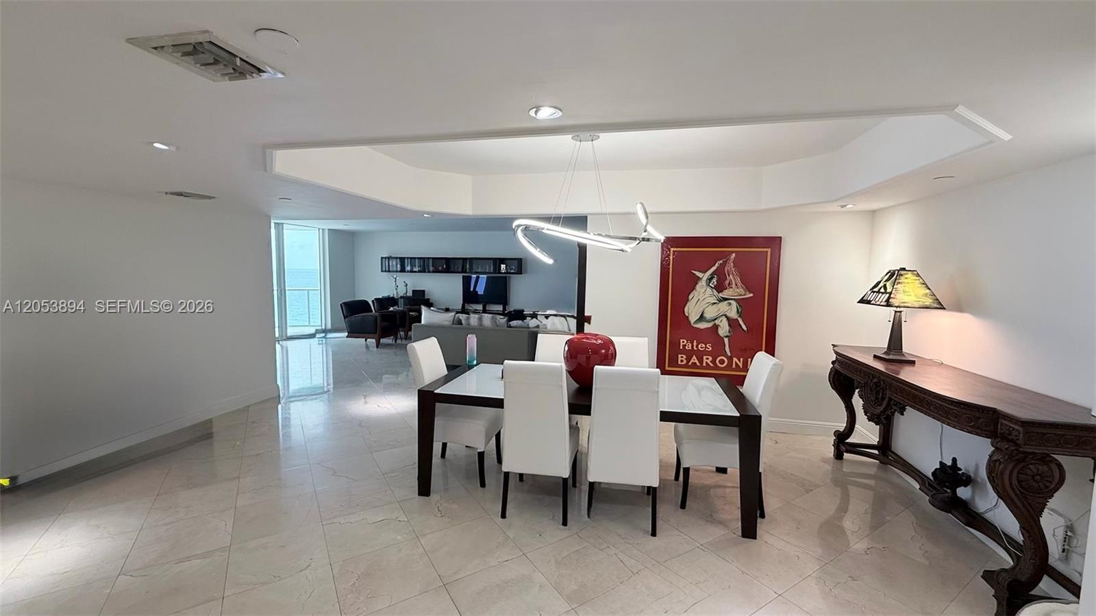 A dining area with a white table and chairs sits in an open-concept living space — 8855 Collins Ave # 11B, Surfside FL 33154, SURFSIDE, FL
