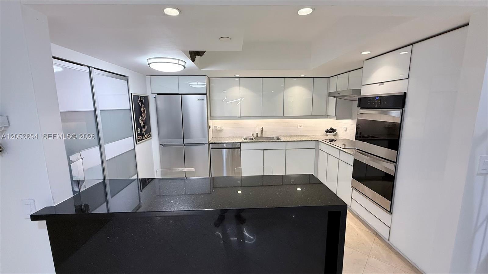 A modern kitchen features white glossy cabinets, stainless steel appliances, and a black granite island — 8855 Collins Ave # 11B, Surfside FL 33154, SURFSIDE, FL