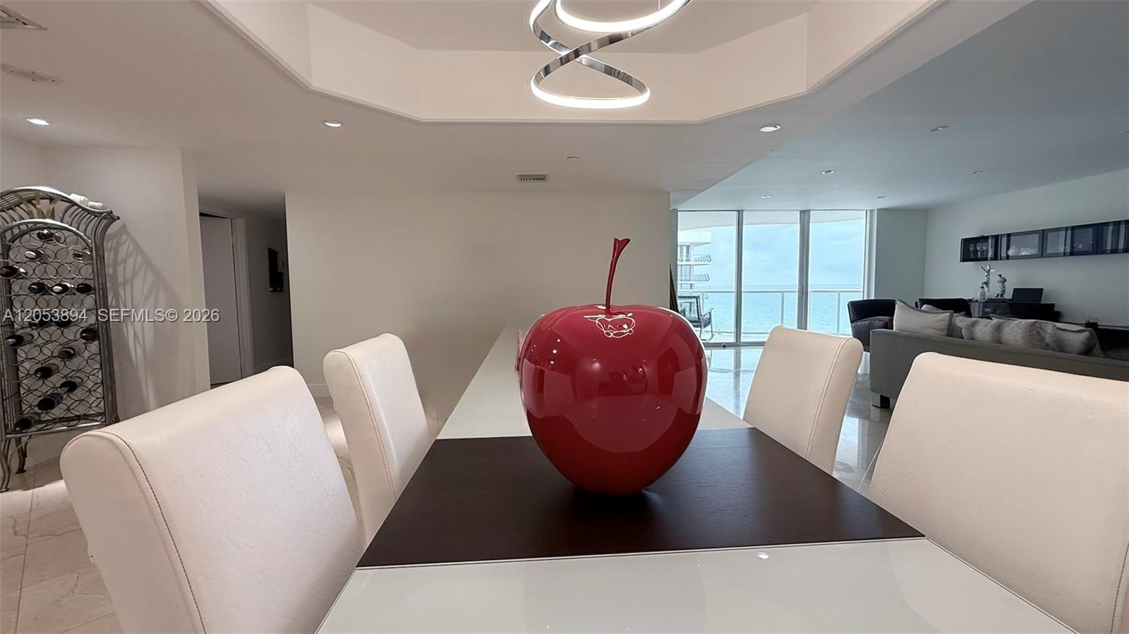 A dining area features a large red apple sculpture on a white table with chairs — 8855 Collins Ave # 11B, Surfside FL 33154, SURFSIDE, FL
