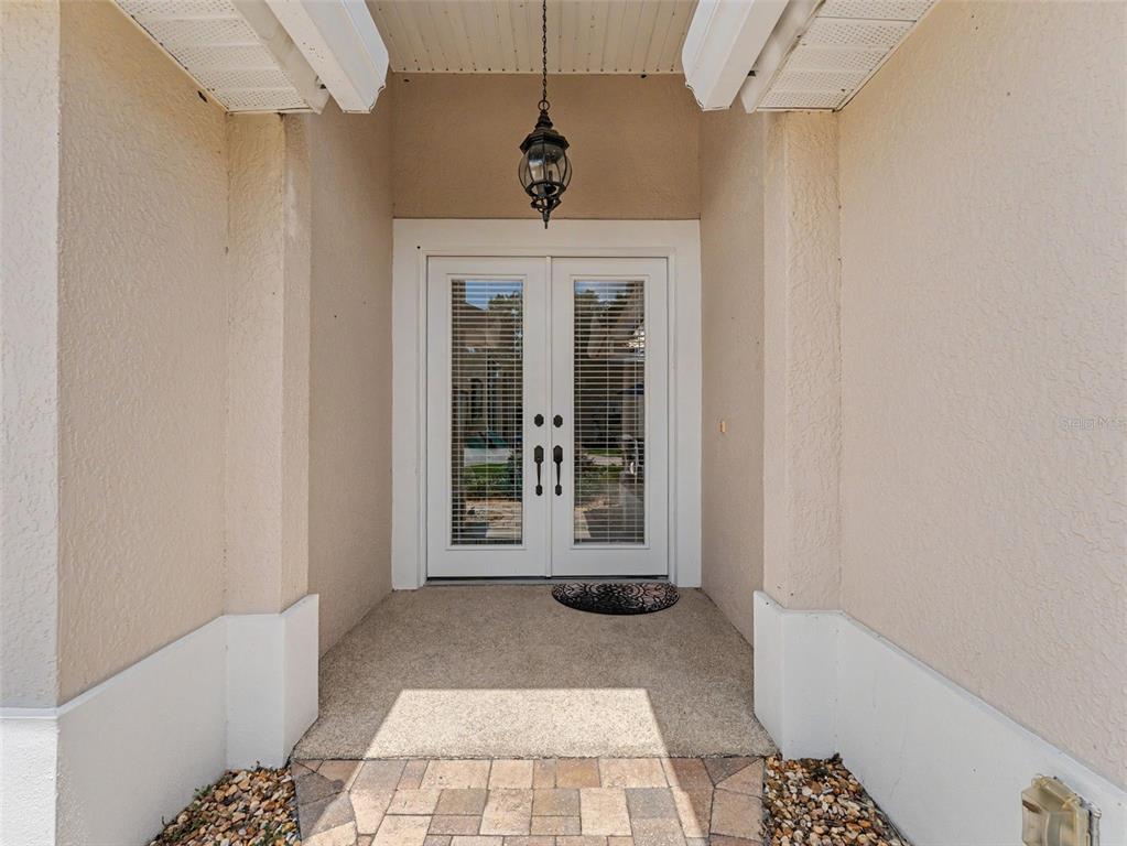 A covered entryway features double glass-paneled doors, a hanging lantern, and a stone-paved walkway — 8910 JERICHO ROAD, WEEKI WACHEE, FL