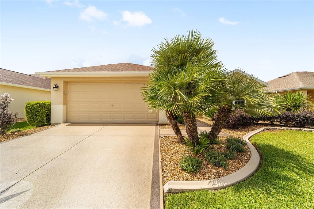 A beige house exterior features a two-car garage, a palm tree, and a concrete driveway — 8588 SE 134TH STREET, SUMMERFIELD, FL