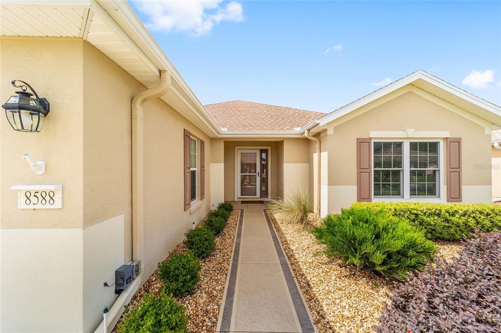 A beige house exterior features a concrete walkway leading to the front entrance — 8588 SE 134TH STREET, SUMMERFIELD, FL